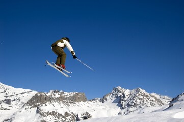 Naklejka na ściany i meble a skier jumping high through a blue sky, above the mountains