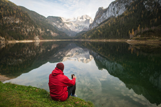 Anonymous man with a cup of coffee sitting near lake