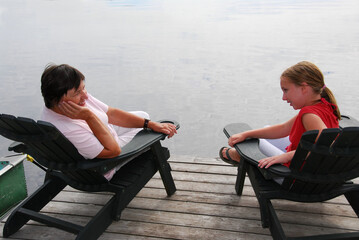 Grandmother and granddaughter sitting in adirondack chairs on a dock having a conversation