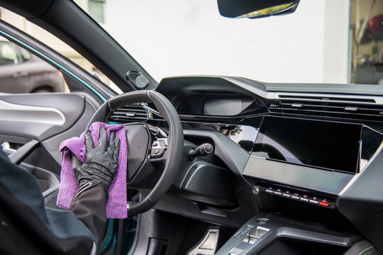 modern car dashboard is beeing carefully cleaned with a micro fiber towel from an professional car detailing service using gloves.. 