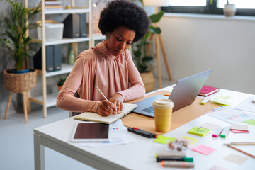 African-American business woman writing in notebook while working in office.