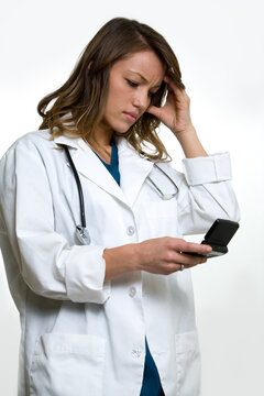 Woman doctor in wearing a doctors lab coat holding up  an open pager with hand on head showing a worried expression