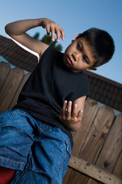 Young asian boy outside beside a tall wooden fence wearing jeans and black tshirt