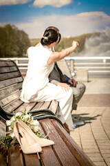 On a summer day, a husband and wife are sitting on a bench in the park, out of focus. A bouquet with a pair of women's shoes on the bench, a romantic couple of newlyweds in the background.