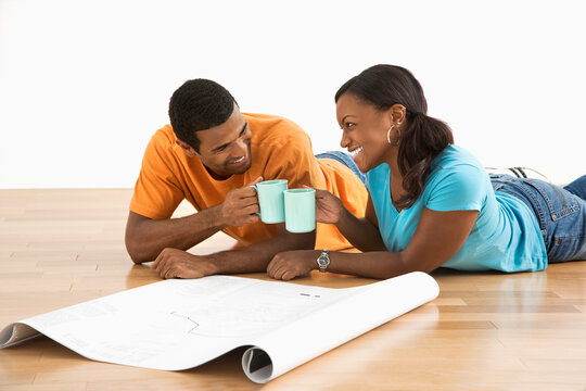 African American male and female couple with architectural  blueprints toasting with their coffee cups.