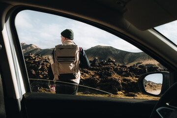 Young Man explores lava valley, mountain volcano from car at road trip