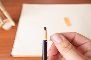 A cartoonist sharpening a charcoal pencil with a notebook and drawing table in the background