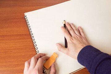 A cartoonist holding an eraser and a charcoal pencil over a sketchbook