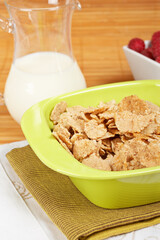 A bowl of cornflakes, milk and raspberries on bamboo mat