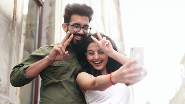 Portrait of young indian couple grimacing taking selfie photograph saving great memories on smartphone mobile phone at city centre Happy relationship concept