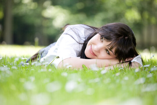 attractive brunette woman relaxing by lying on grass in park