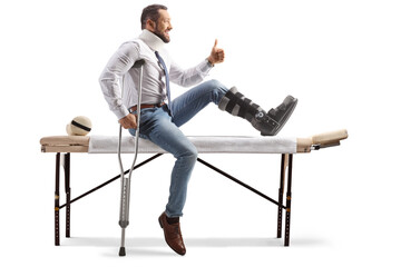 Injured man with an orthopedic boot and neck collar sitting on a therapy table and gesturing thumbs up