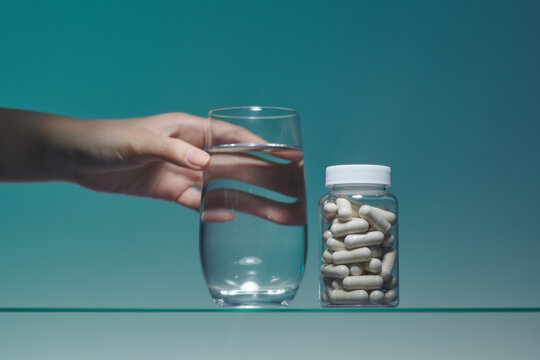 Glass with water against a blue background with pills jar