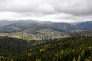 Fototapeta na wymiar Autumn mountains with village under cloudy sky. The beauty of the Carpathians. Tourism and travel