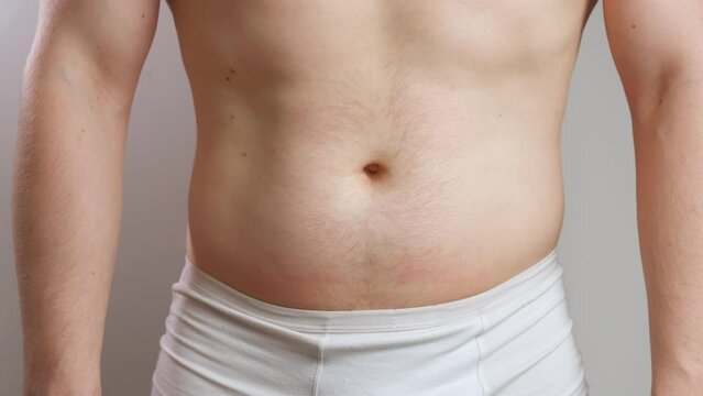 A man with a bare torso in white underpants pulls in a big belly and strains his abs in close-up. The concept of diet and weight loss. Front view
