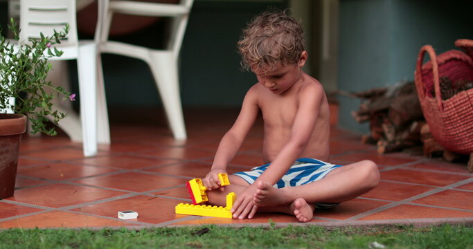 Creative child playing with building blocks outside in summer day. Toddler plays by himself