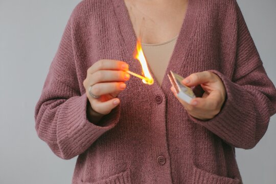 Closeup woman with burning match in hand in gray studio
