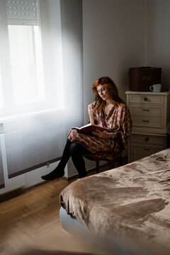 A woman reads near a window in the bedroom