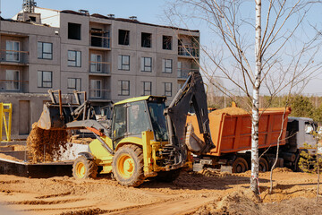 Powerful crawler bulldozer close-up at the construction site. Excavator machine unloading sand during earth moving works. Panel building under construction.