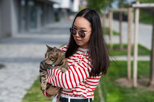 Young woman holding tabby cat in her arms outdoors. 