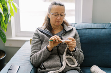 middle aged woman sitting on blue sofa and crocheting a scarf