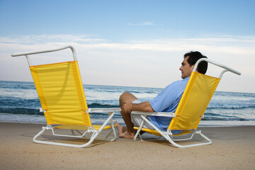 Man sits on the beach alone and looks at an empty chair. Horizontal shot.