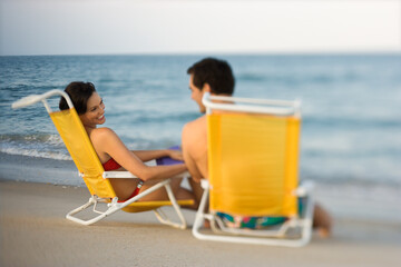 Man and woman smile at each other while sitting in beach chairs. Horizontal shot.