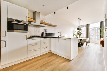 a kitchen and dining area in a house with wood flooring, white cupboards and appliances on the wall