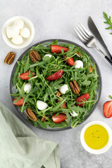 Salad with strawberries, mozzarella balls, arugula and pecans on gray background. Top view.