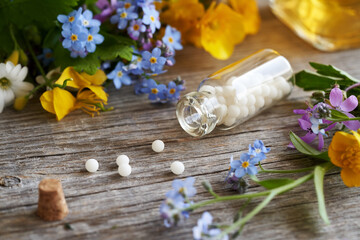 Homeopathic globules with herbs and flowers on a table