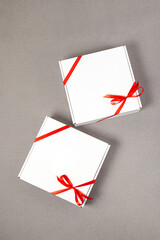 Two white gift boxes with red ribbons on gray background. Mock up