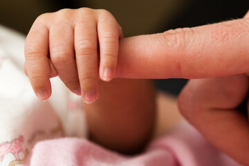Tiny newborn baby fingers wrapped around adult female fingers up close