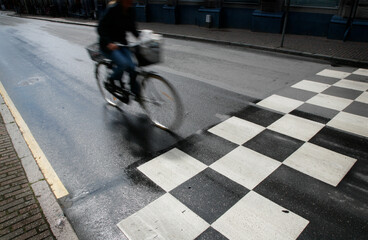 Fototapeta premium Wet morning traffic with speedy cyclist passing crosswalk. Motion blur.