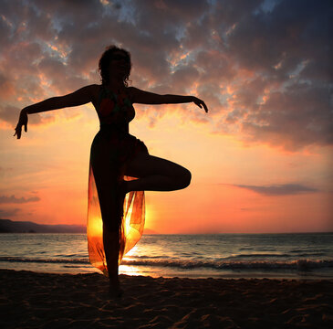Woman doing yoga exercise on the beach at sunset, silhouette