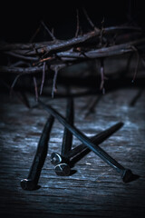 Fototapeta na wymiar Crown thorns and nails as symbol of passion, death and resurrection of Jesus Christ. Selective focus on metal nails. Vertical image.