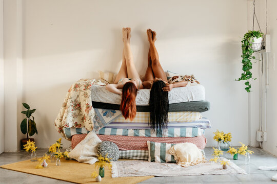 wide shot of two women lying on a pile of mattresses