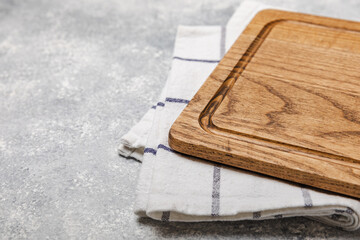Cutting board over kitchen towel on gray kitchen table texture background. Recipe. Kitchenware. Empty modern wooden cutting board. Menu. MOCKUP. Place for text. Place to copy.