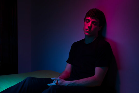 Neon light portrait of young man resting in dark room