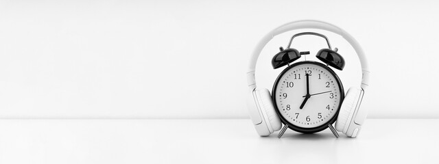 Black alarm clock with headphones on white wall background