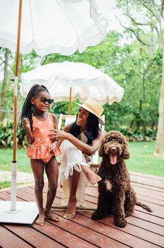 Mom and daughter laugh together sitting on deck under beach umbrella