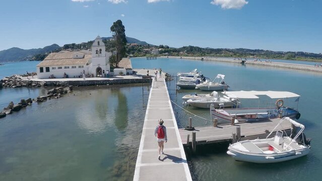 Aerial scene of tourist woman with hat and backpack visiting Vlacherna monastery, Kanoni, Corfu, Greece, slow motion
