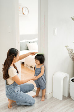 Young woman measuring her daughter's height indoors