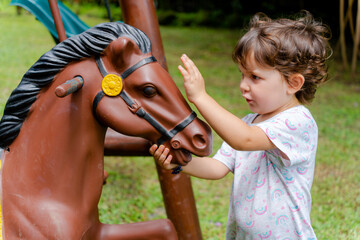 Happy little girl with horse toy in playground