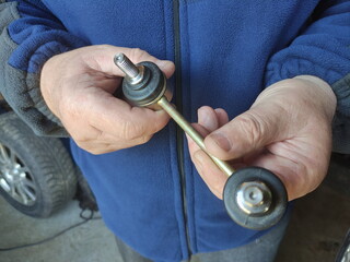 Car stabilizer link in serviceman hands on car wheel background