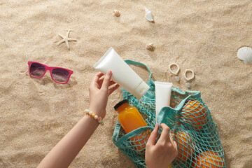Women's hands put sunscreen into string bag on beach sand