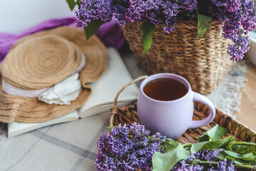 Obraz na płótnie Canvas Cup of tea, straw hat and lilac basket, spring still life