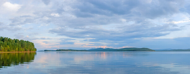 Beautiful clouds at sunset panorama of the lake with mountains on the horizon reflected on the water. © Dmitry