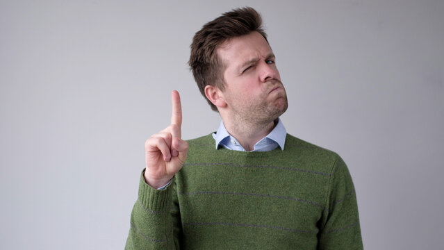 European young man shakes his head in disagreement and says no, pointing his finger upwards