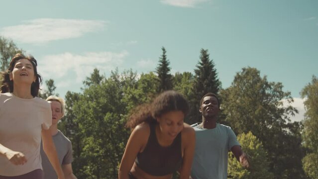 Slowmo of young diverse team of runners crossing red finish line on outdoor track in summer