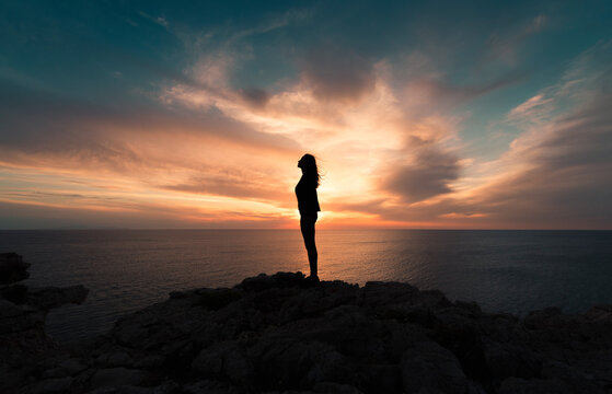 Standing woman on cliff edge during sunset